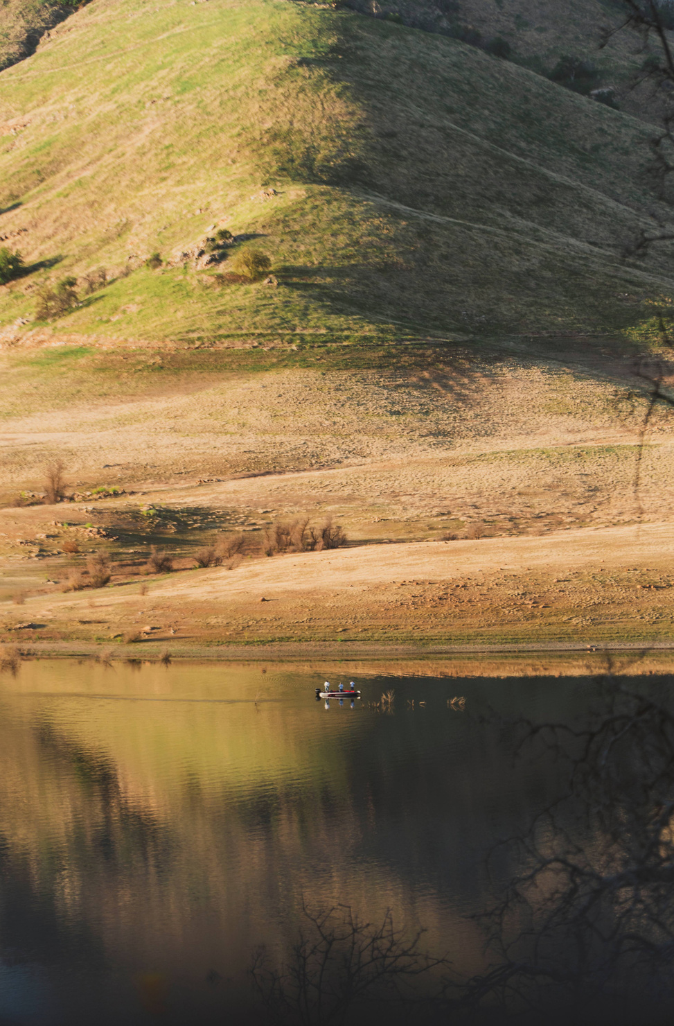 Fisherman on small boat at Lake Kaweah, backed by a scenic green and yellow mountain.