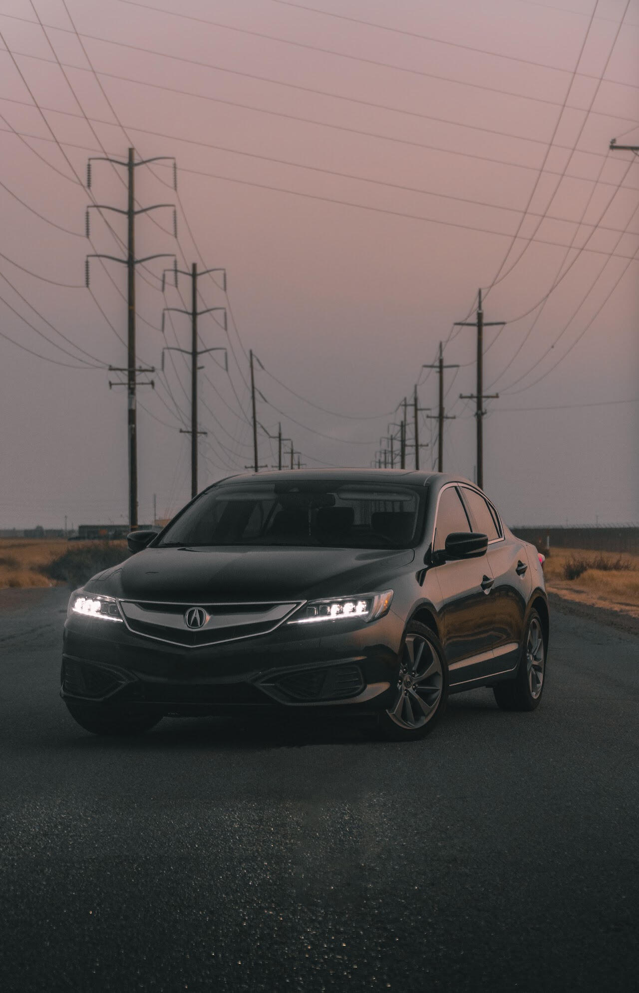 A black Acura on an empty road with vibrant yellow grass growing alongside